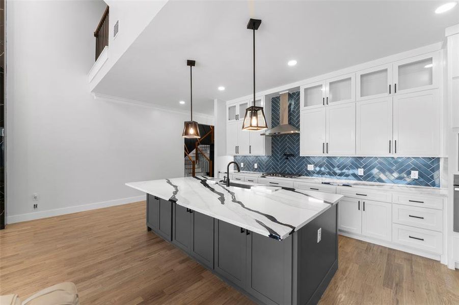 Kitchen featuring backsplash, white cabinets, glass insert cabinets, light stone countertops, and decorative light fixtures Kitchen featuring backsplash, white cabinets, glass insert cabinets, light stone countertops, and decorative light fixtures