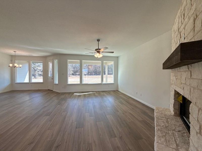 Unfurnished living room with dark wood-style floors, a stone fireplace, a chandelier, and ceiling fan