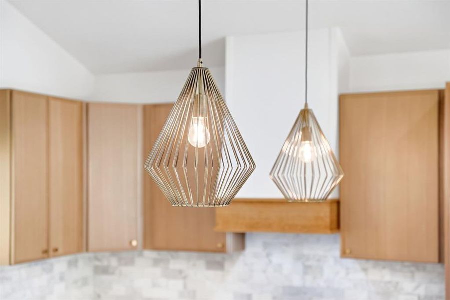 Geometric pendant lighting illuminating a kitchen area featuring light wood-finish cabinetry and a light-toned tile backsplash