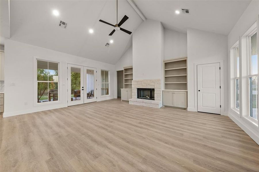 Unfurnished living room with high vaulted ceiling, french doors, beamed ceiling, a fireplace, and light wood-style floors Unfurnished living room with high vaulted ceiling, french doors, beamed ceiling, a fireplace, and light wood-style floors