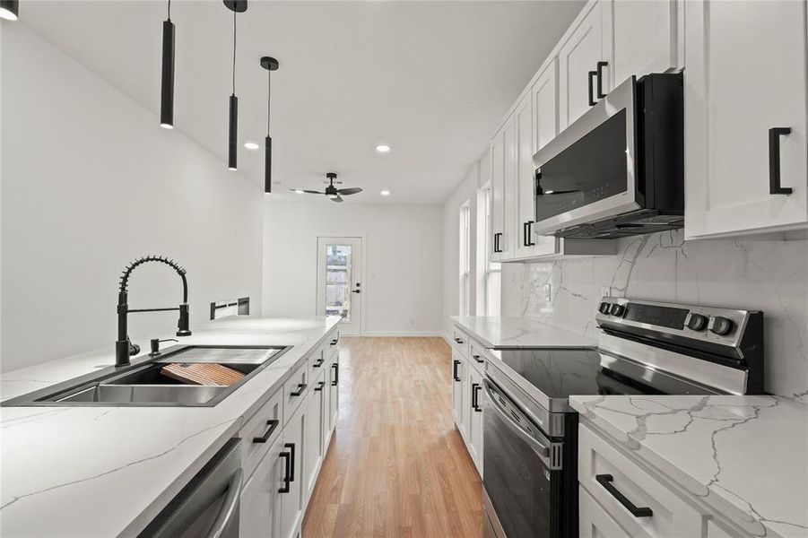 Kitchen featuring hanging light fixtures, appliances with stainless steel finishes, sink, and white cabinets