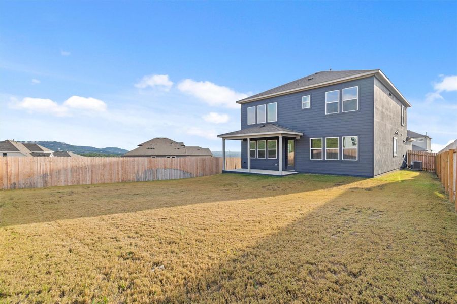 Rear view of house with central AC unit and a lawn