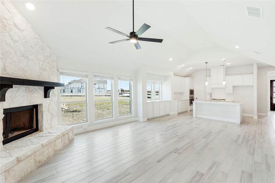 Open living area with stone fireplace, vaulted ceiling, and open-concept kitchen with white cabinets and island