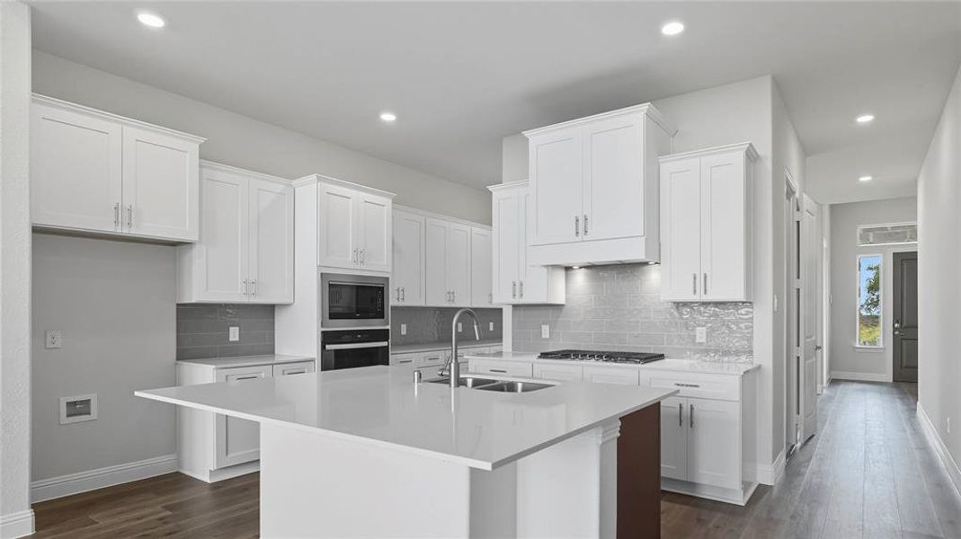 Kitchen with white cabinets, an island with sink, backsplash, dark wood-type flooring, and stainless steel appliances