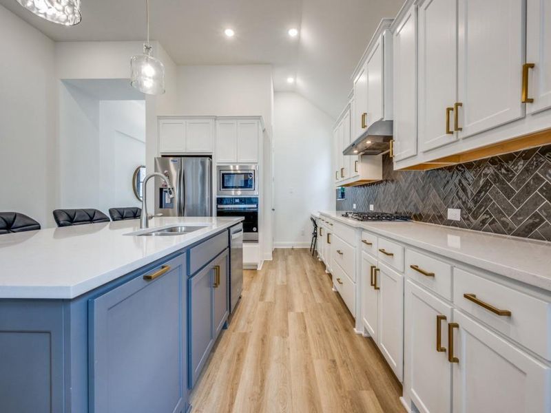 Kitchen with backsplash, a sink, under cabinet range hood, stainless steel appliances, and blue cabinetry