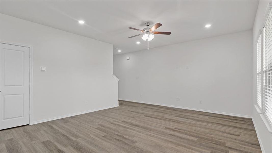 Spacious room featuring wood-finish flooring, white walls, and a ceiling fan with integrated lighting Spacious room featuring wood-finish flooring, white walls, and a ceiling fan with integrated lighting