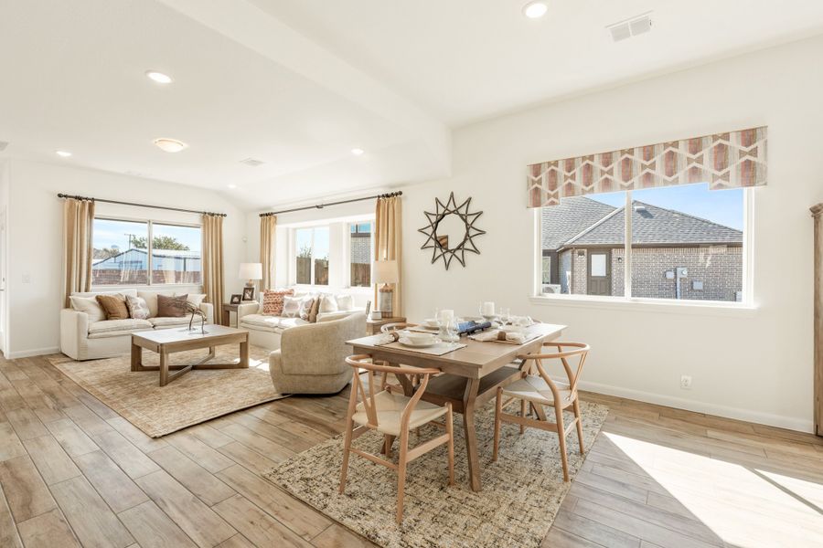 Open-concept living and dining area with wood-look floors, neutral furniture, and multiple windows letting in natural light.