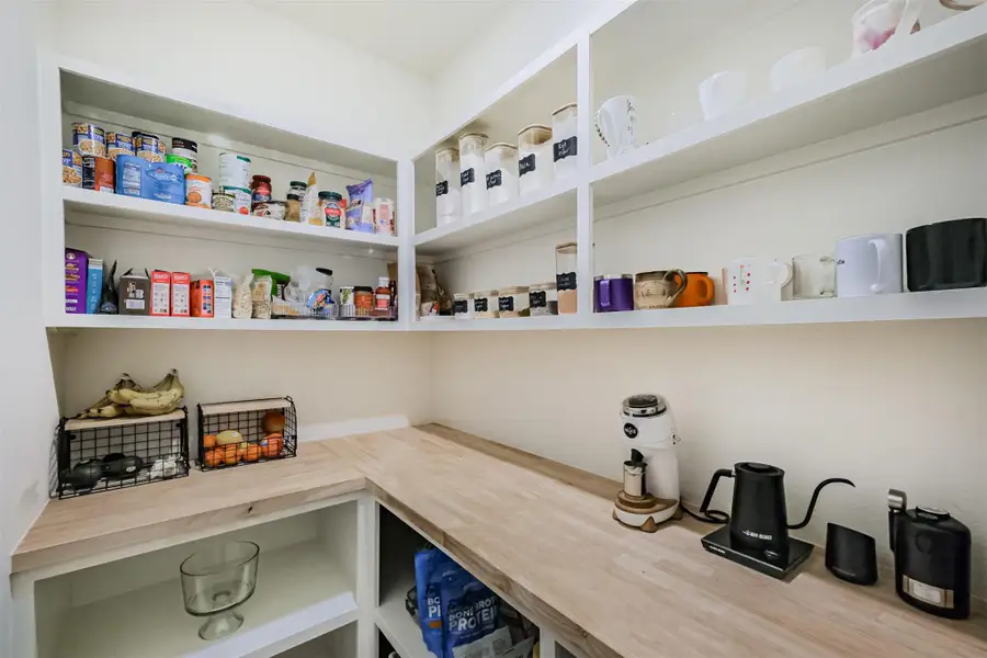 Organized walk-in pantry/coffee station with white open shelving, butcher block countertop, and plenty of storage.