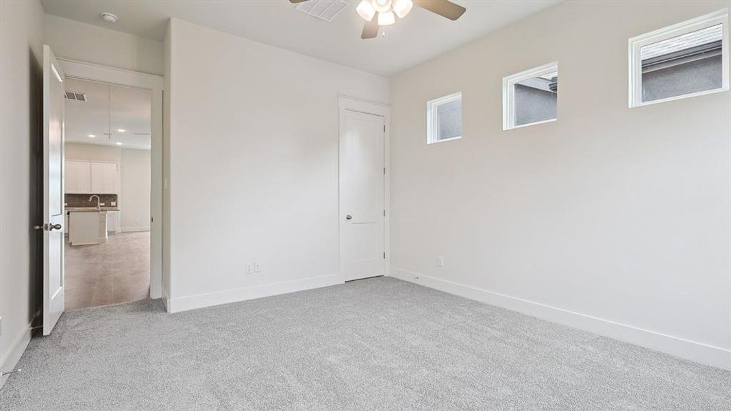 Carpeted room with ceiling fan, white walls, and three upper windows