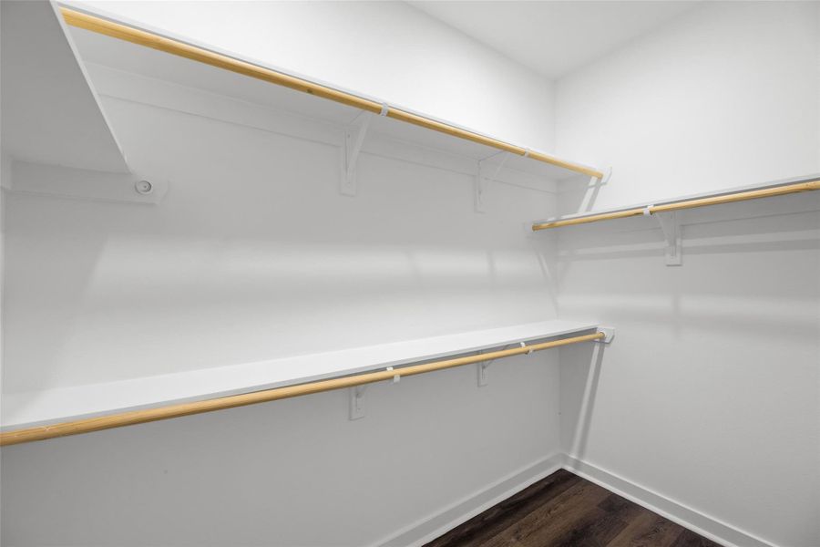 Roomy walk-in closet with multiple wooden shelves and rods, ideal for organizing clothes and accessories. Bright, white walls and dark hardwood flooring enhance the modern look. Roomy walk-in closet with multiple wooden shelves and rods, ideal for organizing clothes and accessories. Bright, white walls and dark hardwood flooring enhance the modern look.
