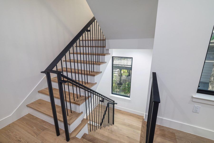 Modern staircase featuring wood-finish treads and risers, black metal railings, and white walls