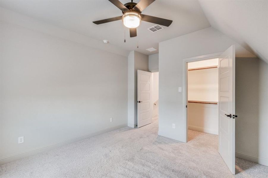 Unfurnished bedroom with ceiling fan, lofted ceiling, a walk in closet, light carpet, and a closet