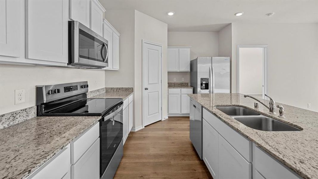 Kitchen with stainless steel appliances, white cabinets, wood finished floors, light stone countertops, and recessed lighting