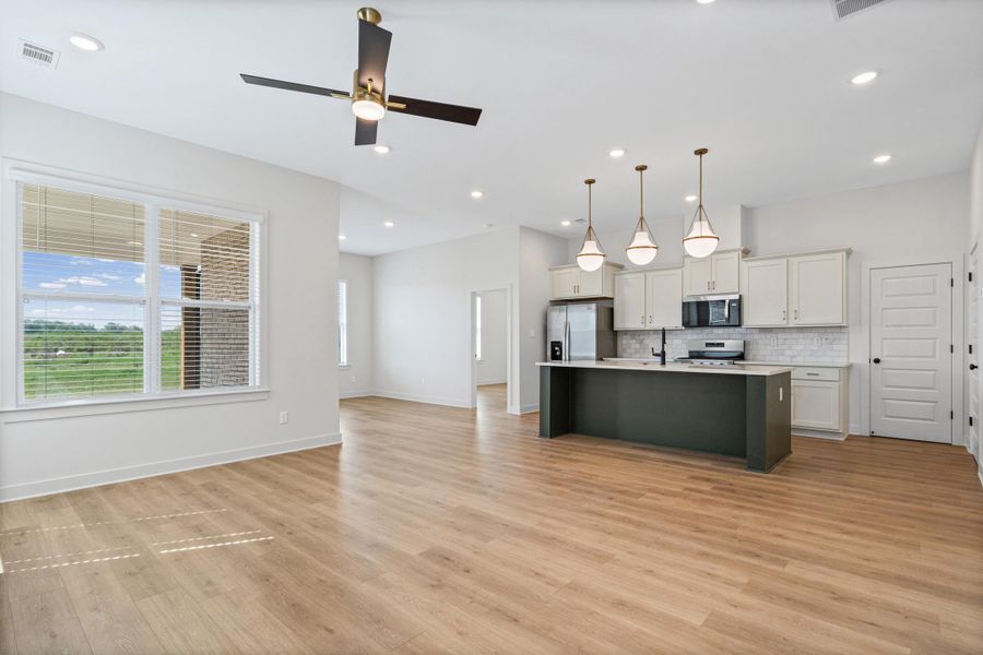 Two tone kitchen with open floor plan, light countertops, a center island with sink, ceiling fan, and stainless steel appliances