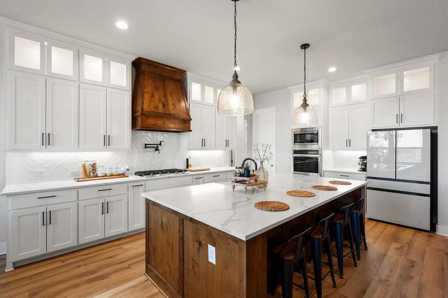 Kitchen with glass insert cabinets, white cabinetry, appliances with stainless steel finishes, a breakfast bar, and backsplash