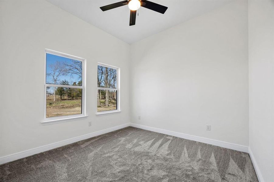 Room featuring two windows with white trim, vaulted ceiling, ceiling fan with light fixture, light gray carpet, and white baseboards Room featuring two windows with white trim, vaulted ceiling, ceiling fan with light fixture, light gray carpet, and white baseboards
