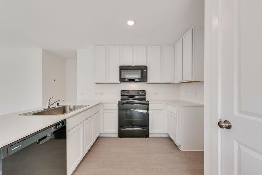 Kitchen featuring black appliances, white cabinetry, a peninsula, light wood-style floors, and recessed lighting