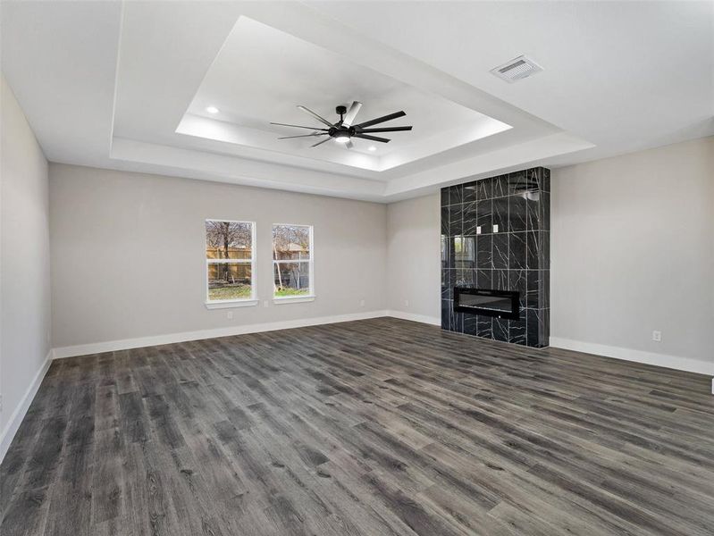 Unfurnished living room featuring a tray ceiling, a premium fireplace, ceiling fan, and dark wood-type flooring