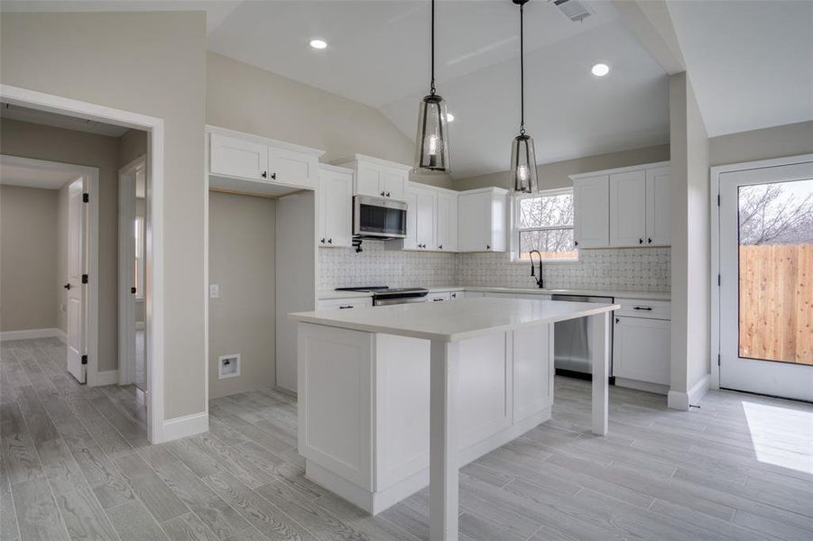 Kitchen featuring a kitchen island, light countertops, vaulted ceiling, light wood-style flooring, and appliances with stainless steel finishes