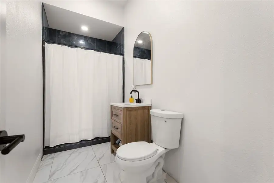 Full bath featuring a shower with curtain, light marble finish flooring, and vanity