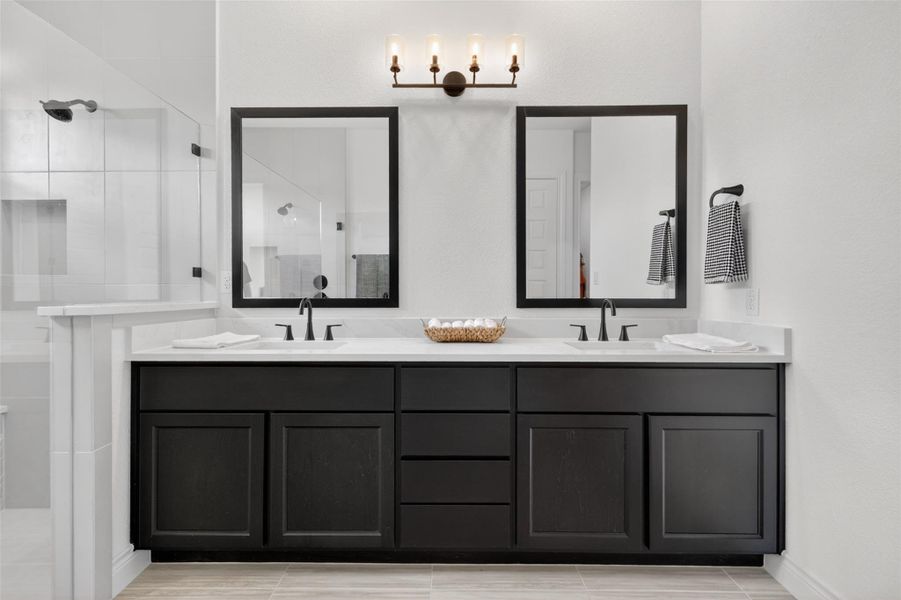 Dual vanities with sleek dark cabinetry and polished countertops await in this contemporary primary bathroom. Dual vanities with sleek dark cabinetry and polished countertops await in this contemporary primary bathroom.