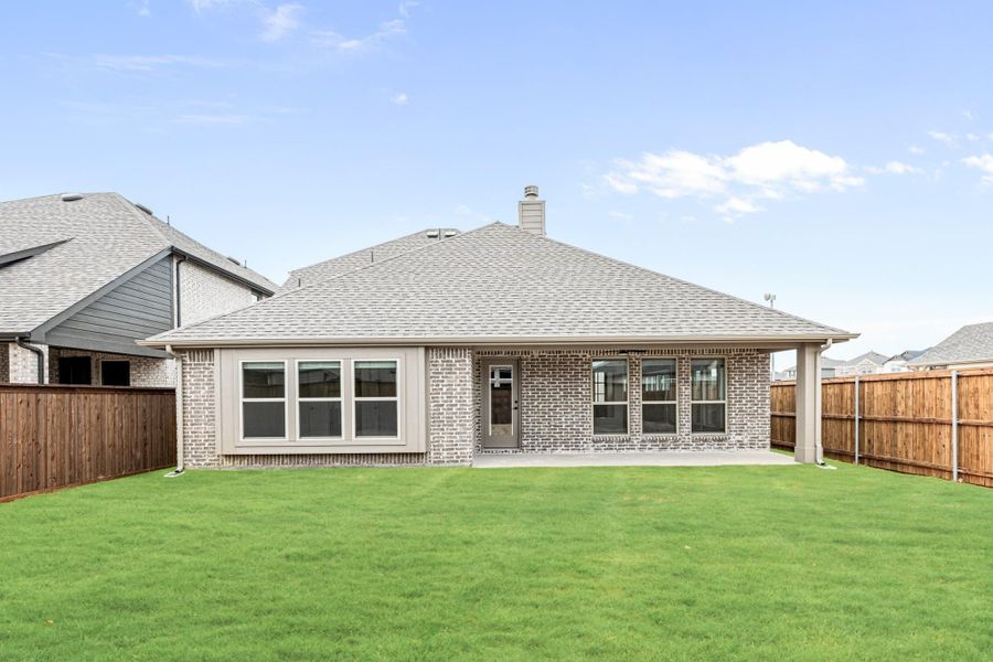 Rear view of single-story brick home with covered patio, green lawn, and wood privacy fence Rear view of single-story brick home with covered patio, green lawn, and wood privacy fence