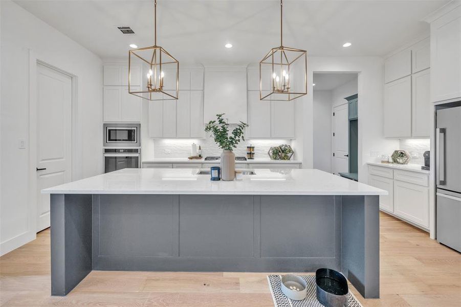 Kitchen featuring a kitchen island with sink, light hardwood / wood-style flooring, stainless steel appliances, and decorative light fixtures