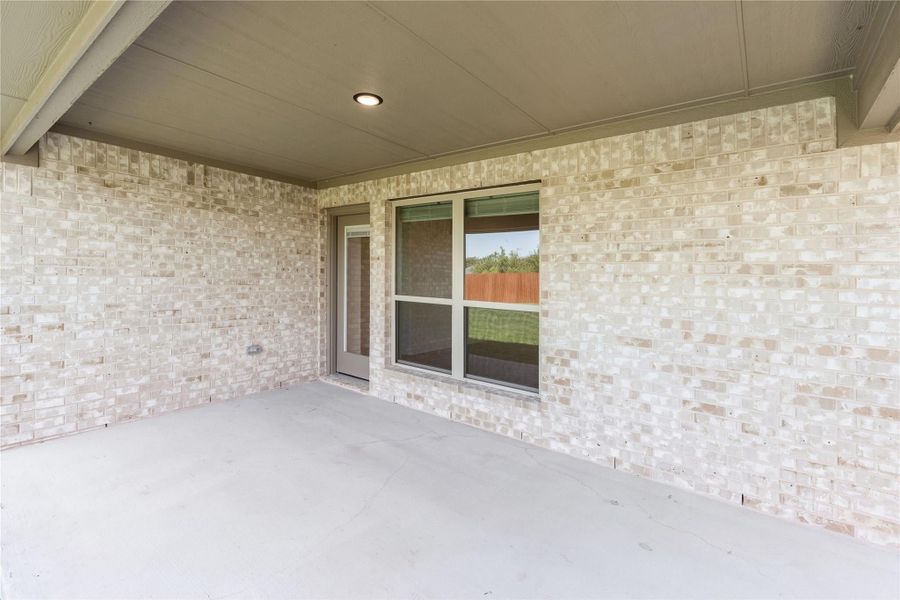 Covered back patio with concrete floor, light brick walls, and sliding glass door with screen