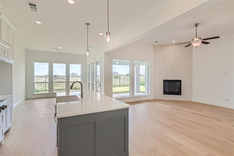 Kitchen featuring light hardwood / wood-style floors, a fireplace, ceiling fan, an island with sink, and pendant lighting