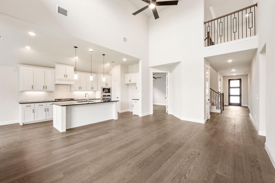 Open-concept living area with white kitchen, large island, hardwood floors, and two-story ceiling with ceiling fan Open-concept living area with white kitchen, large island, hardwood floors, and two-story ceiling with ceiling fan
