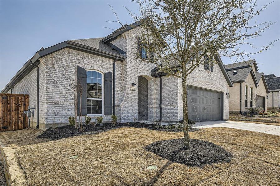 French country inspired facade with brick siding, concrete driveway, roof with shingles, and fence