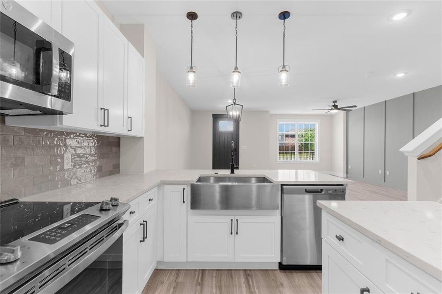 Modern kitchen featuring white cabinetry, stainless steel appliances, a farmhouse sink, subway tile backsplash, and quartz countertops