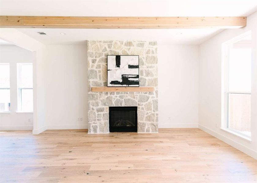 Unfurnished living room featuring beamed ceiling, a fireplace, and light hardwood / wood-style floors