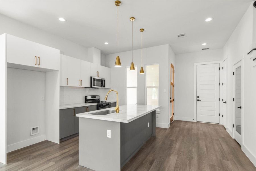 Bright modern kitchen featuring a large island with quartz countertops, sleek cabinetry, and gold accents. Bright modern kitchen featuring a large island with quartz countertops, sleek cabinetry, and gold accents.