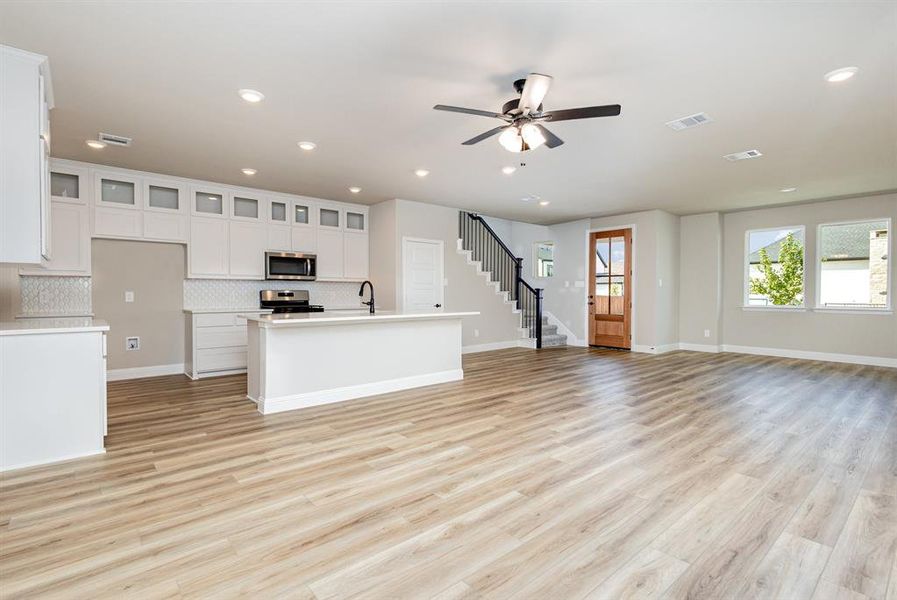 Unfurnished living room with light wood finished floors, ceiling fan, recessed lighting, and stairway