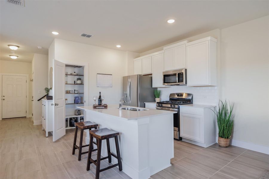 Kitchen with stainless steel appliances, white cabinetry, a breakfast bar, a kitchen island with sink, and backsplash Kitchen with stainless steel appliances, white cabinetry, a breakfast bar, a kitchen island with sink, and backsplash