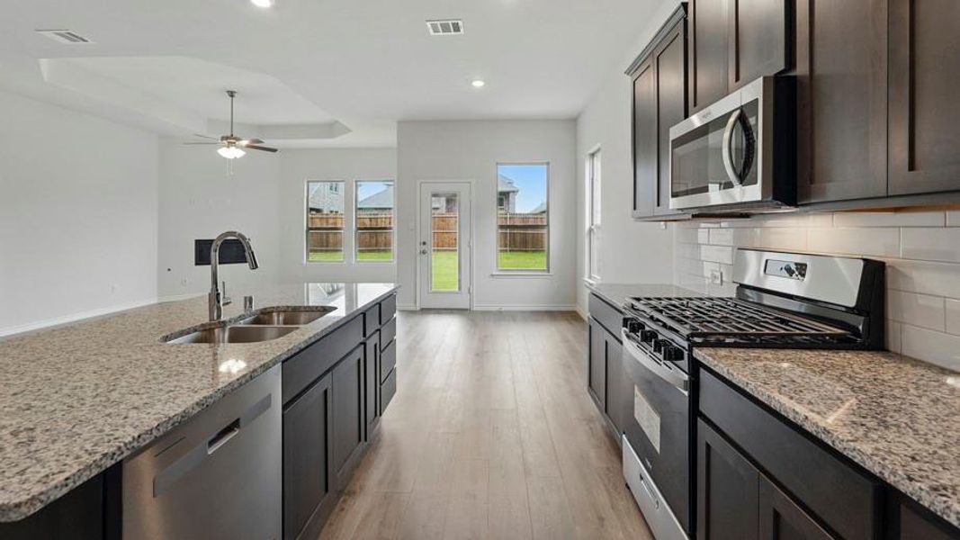 Modern kitchen featuring granite countertops, dark wood-finish cabinetry, stainless steel appliances, and a subway tile backsplash