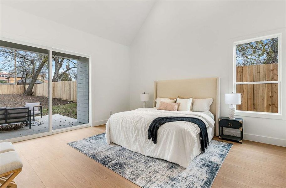Bedroom with access to outside, multiple windows, high vaulted ceiling, and light wood-style floors