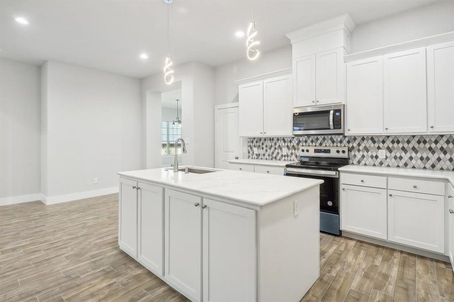 Kitchen featuring light wood-type flooring, a kitchen island with sink, white cabinets, appliances with stainless steel finishes, and decorative light fixtures