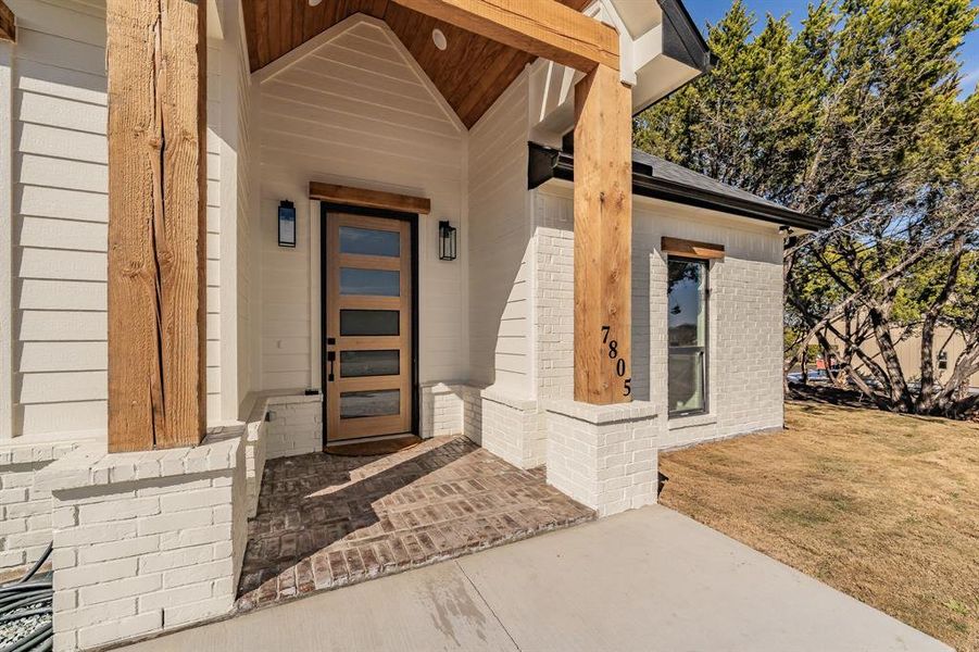 Property entrance featuring brick siding, covered porch, and a lawn