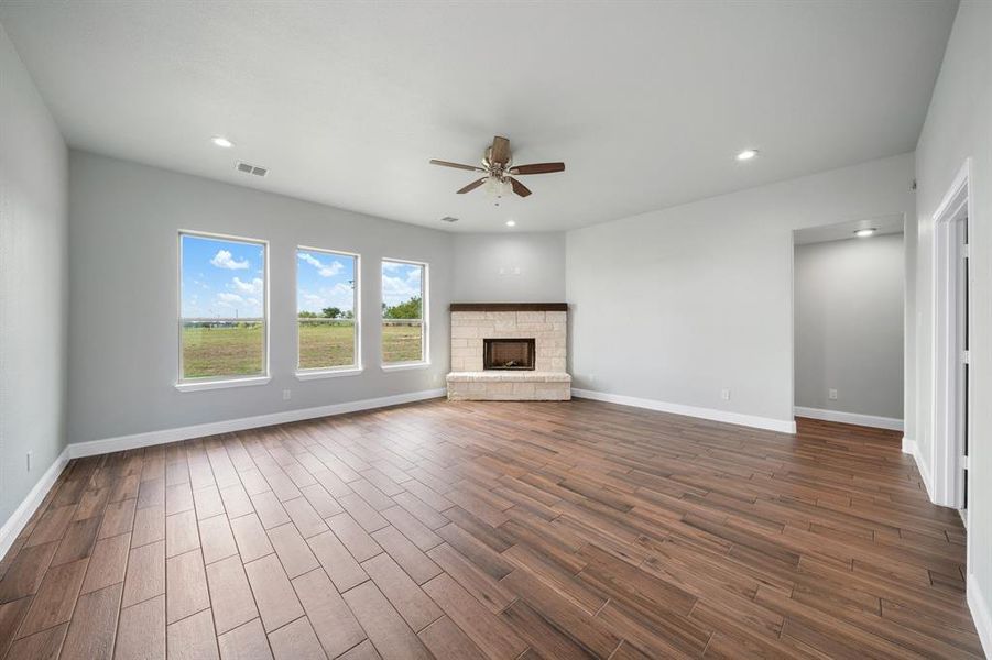 Unfurnished living room with dark hardwood / wood-style flooring, a stone fireplace, and ceiling fan