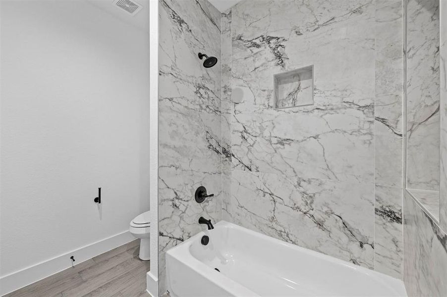 Bathroom with tiled shower / bath combo, wood-type flooring, and toilet