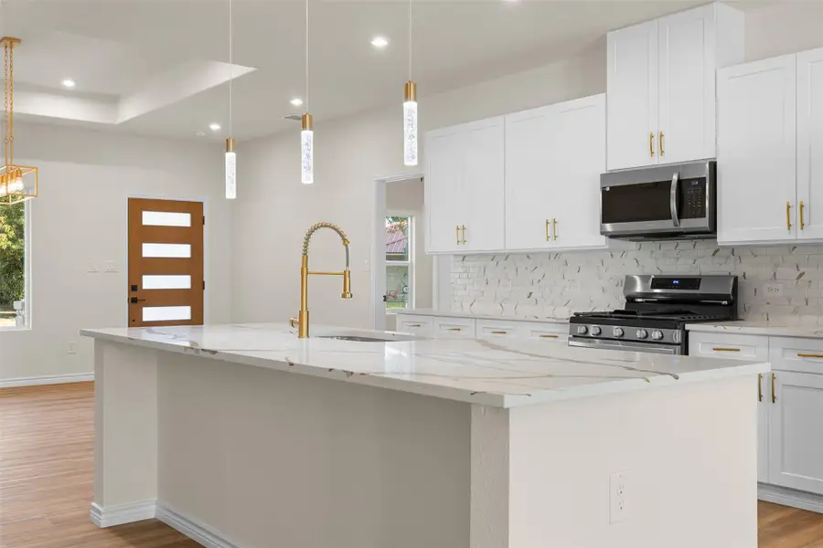 Kitchen featuring light stone countertops, light wood finished floors, decorative backsplash, white cabinets, and stainless steel appliances Kitchen featuring light stone countertops, light wood finished floors, decorative backsplash, white cabinets, and stainless steel appliances