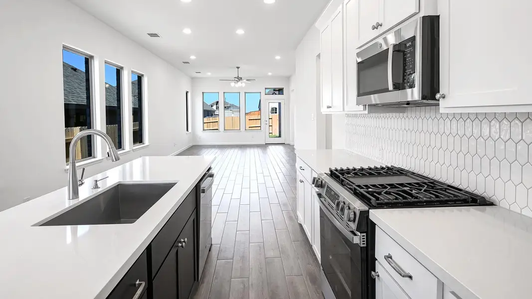 Kitchen with dark cabinetry, wood tiled floors, appliances with stainless steel finishes, white cabinetry, and recessed lighting Kitchen with dark cabinetry, wood tiled floors, appliances with stainless steel finishes, white cabinetry, and recessed lighting