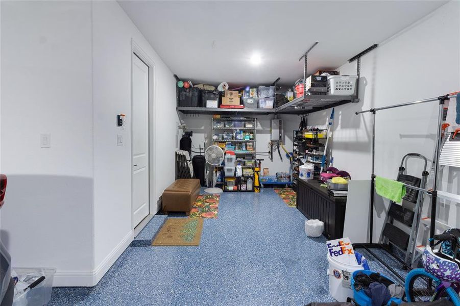 Garage featuring a blue epoxy floor, overhead storage racks, white painted walls, interior access door, and baseboard trim