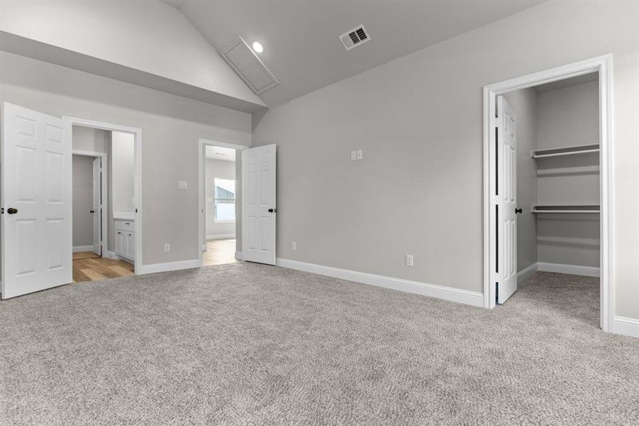 Unfurnished bedroom featuring light colored carpet, a walk in closet, high vaulted ceiling, baseboards, and a closet Unfurnished bedroom featuring light colored carpet, a walk in closet, high vaulted ceiling, baseboards, and a closet