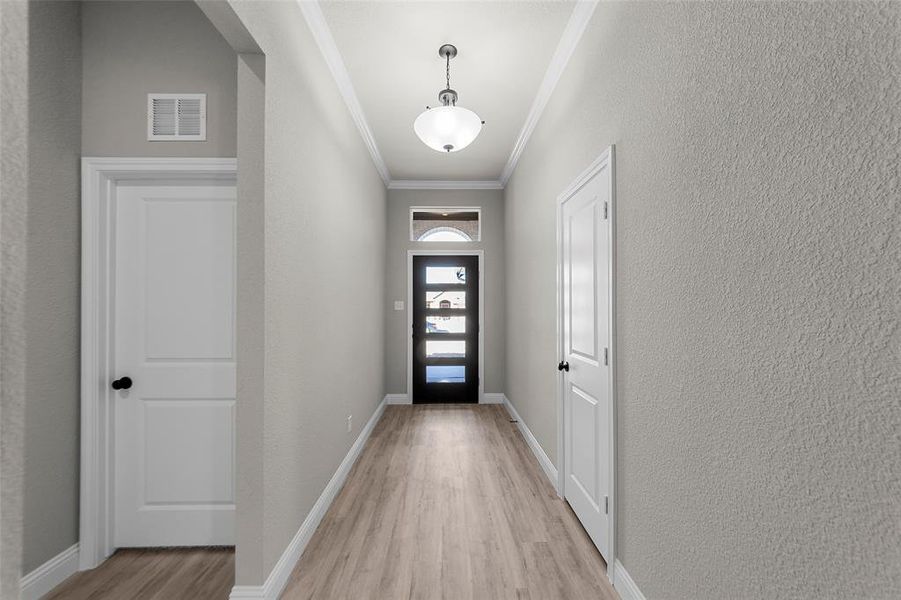 Doorway featuring crown molding, a textured wall, and wood finished floors