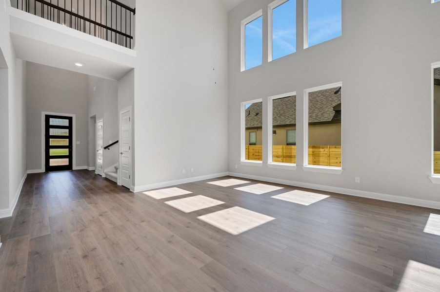 Unfurnished living room featuring wood finished floors, healthy amount of natural light, and a towering ceiling
