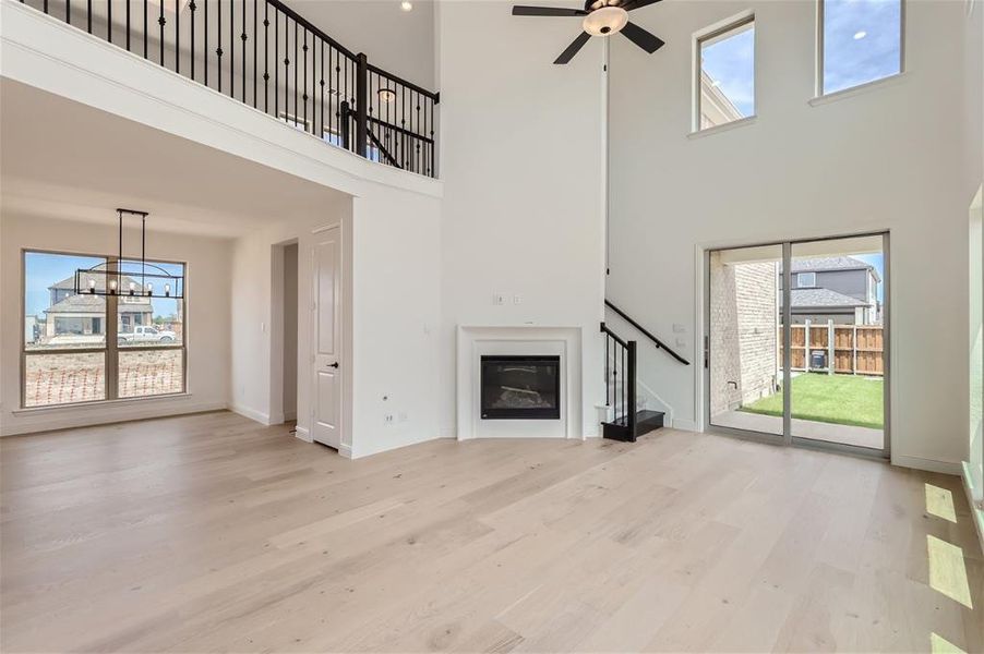 Unfurnished living room featuring a high ceiling, ceiling fan with notable chandelier, and light hardwood / wood-style floors