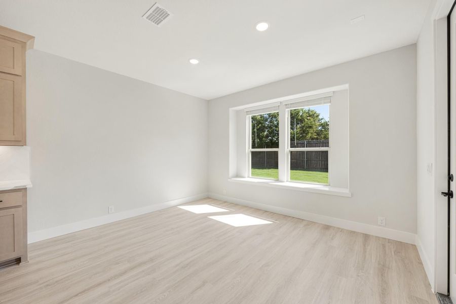 Empty room with light wood floors, white walls, and a window overlooking a fenced backyard
